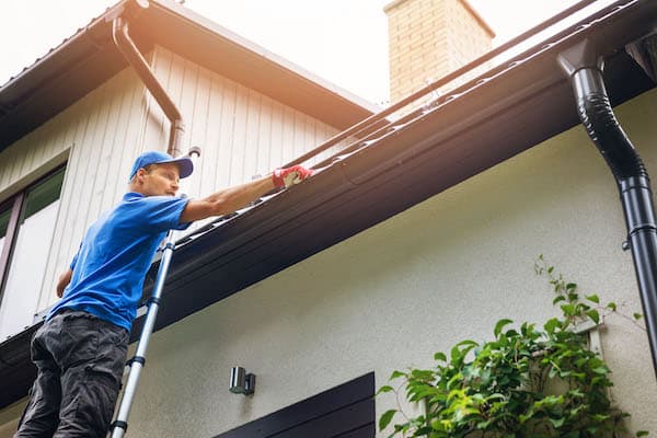 man on ladder cleaning house gutter from leaves and dirt roofing pros centennial colorado